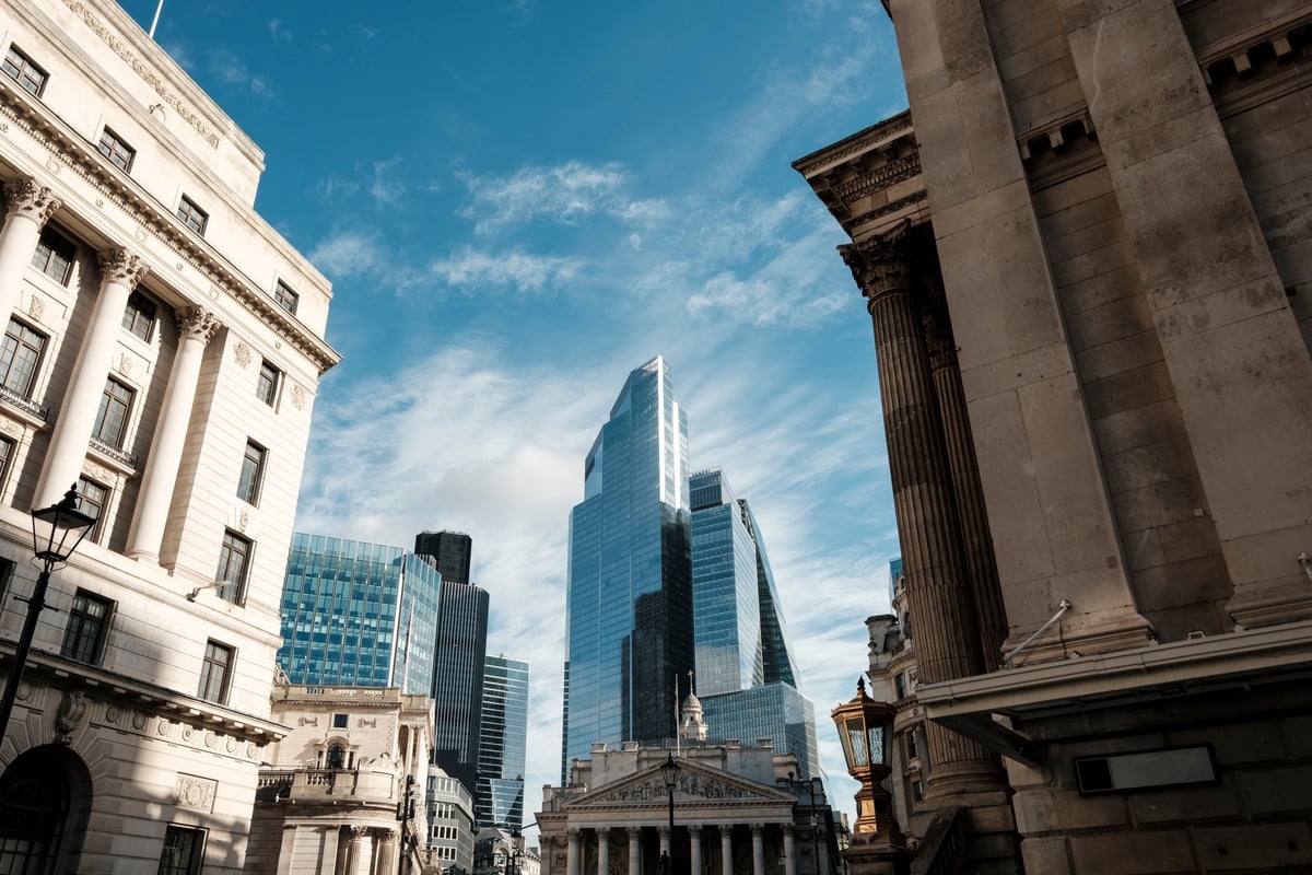 London cityscape showing historic stone buildings framing modern glass skyscrapers in the financial district under a bright blue sky