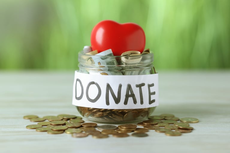 Donation jar with pound sterling banknotes, coins and red decorative heart on wooden table, representing UK charitable giving and Gift Aid tax relief