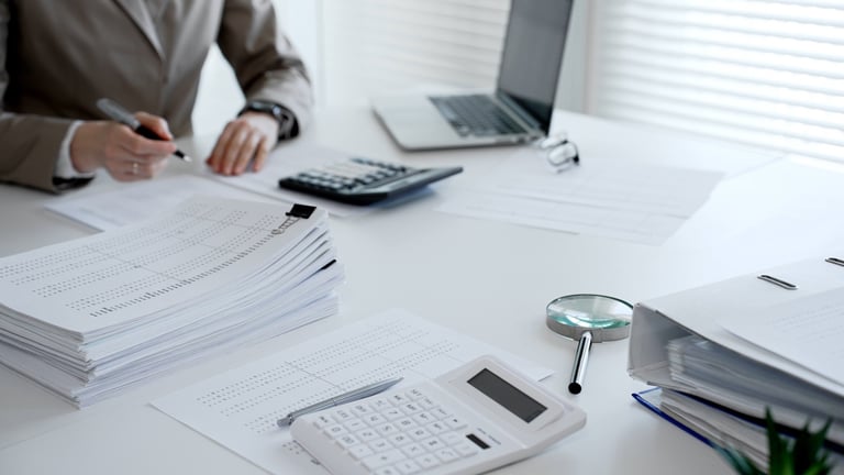 Accountants or auditors collaborating, analyzing financial statements, and preparing tax returns with calculators and a laptop on a white desk. Audit and taxes theme in business